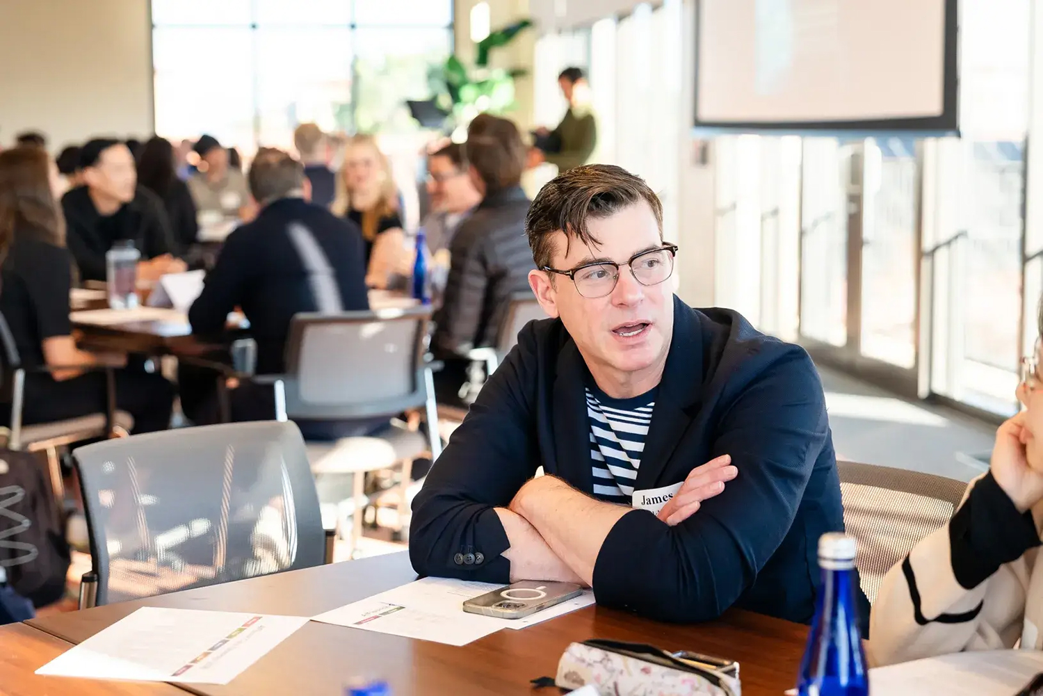 James Buckhouse sits at a conference table with his arms crossed and engaged in conversation.