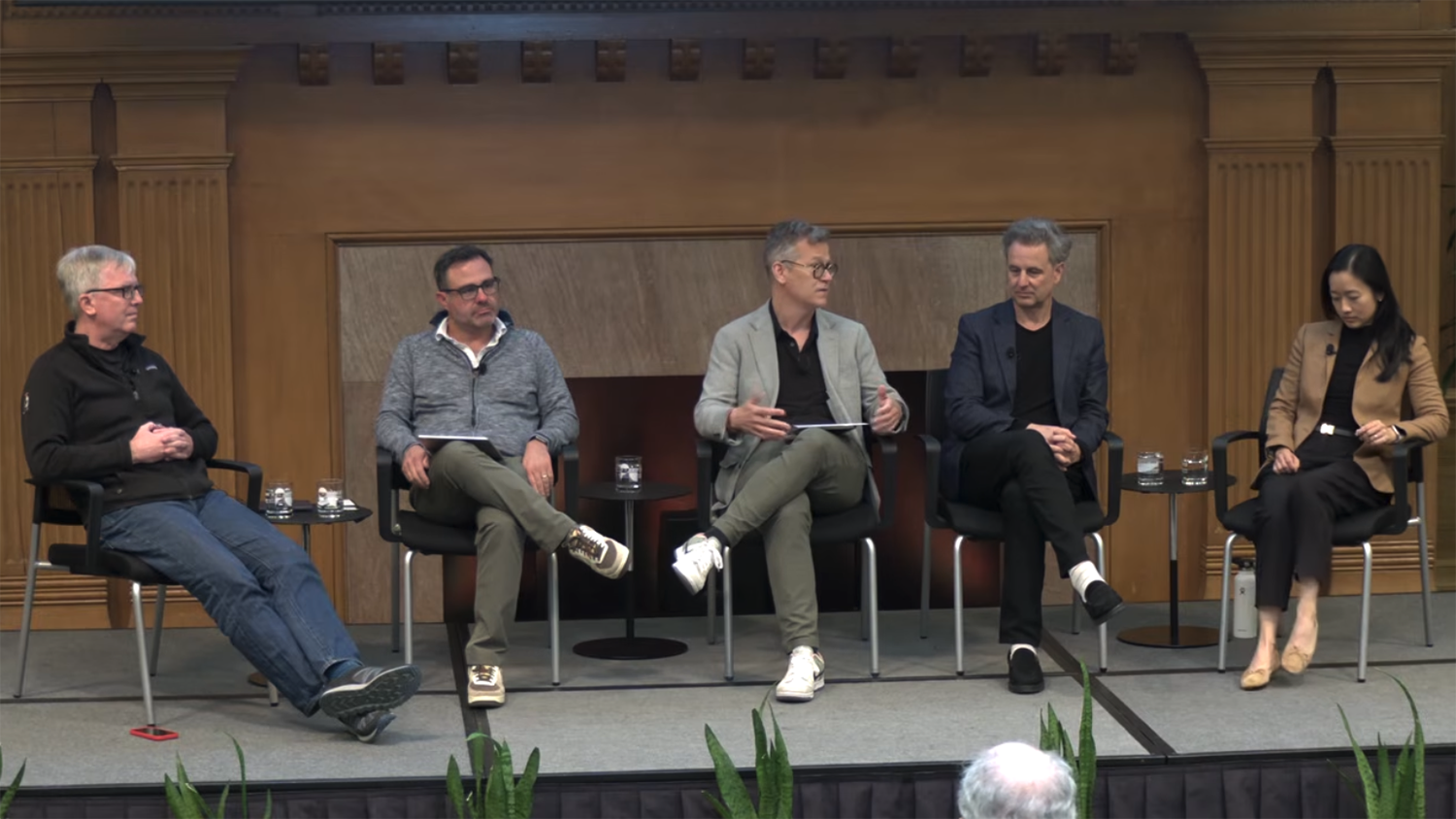 Five panelists seated on stage engaged in a discussion at a formal event.
