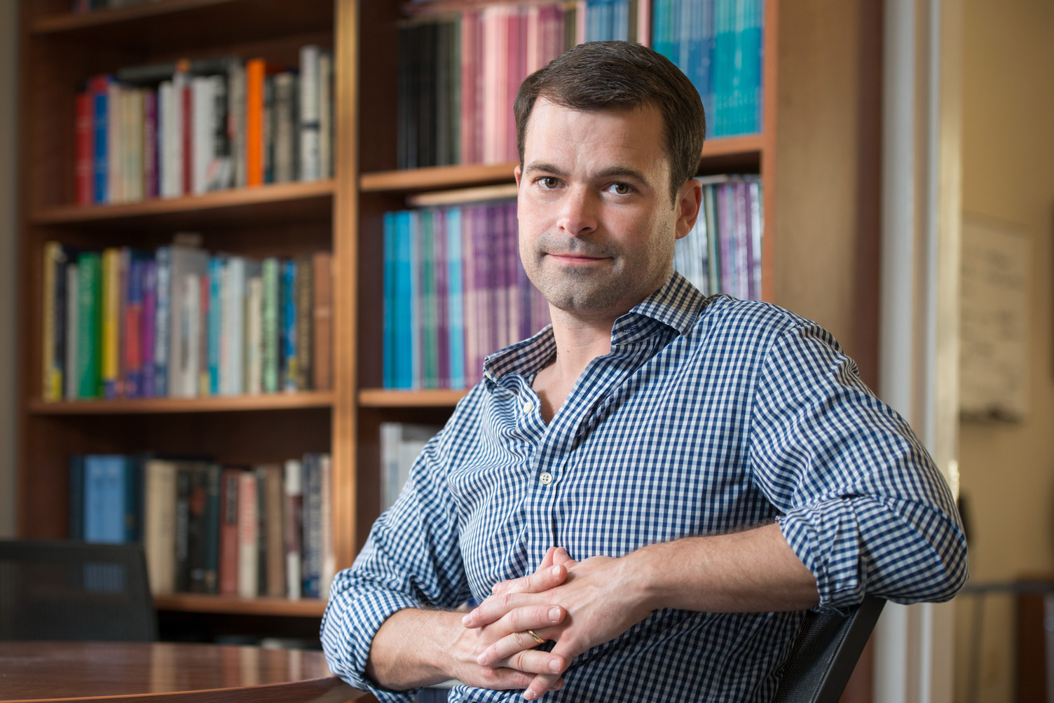 Robb Willer sitting at a table with his hands clasped in front of a shelf filled with books.