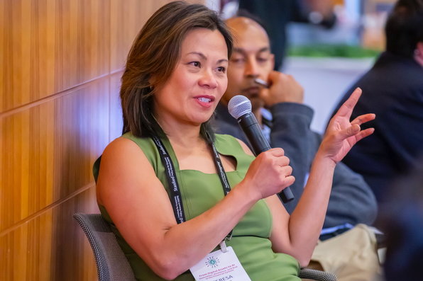 Teresa Kong in a green dress speaks into a microphone while seated, actively engaging in discussion.