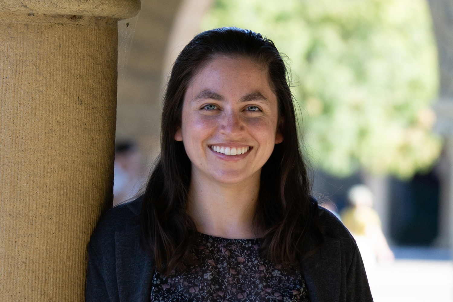 Guzman with long dark hair smiling at the camera while standing near a sandstone column.