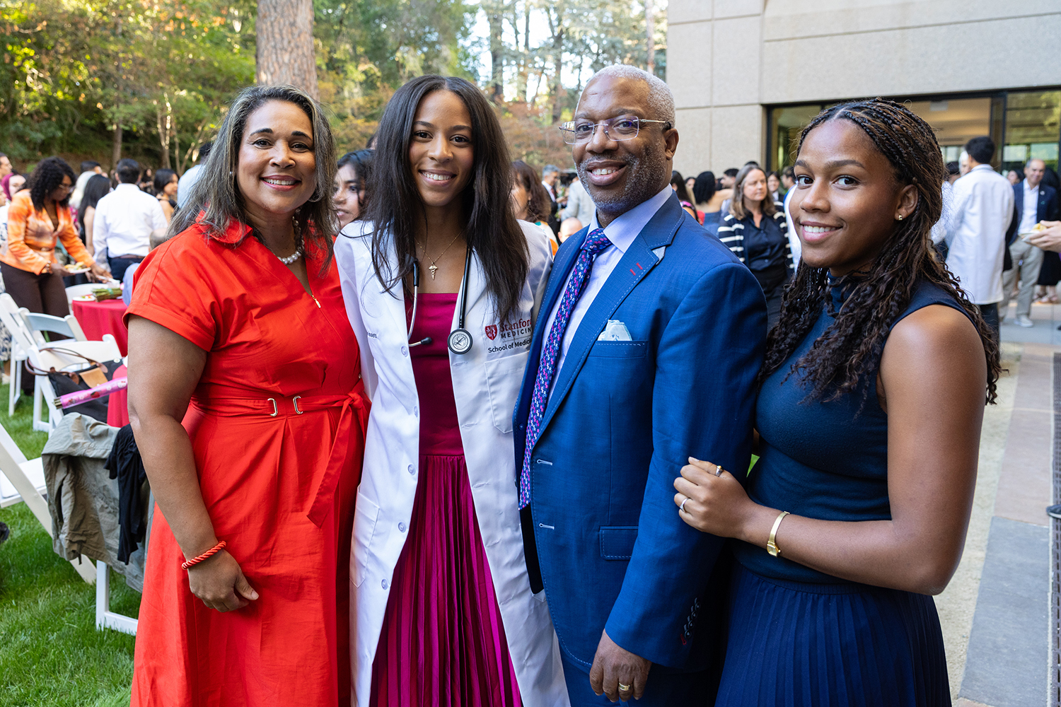 A medical student in a white coat poses with three family members at an outdoor reception.