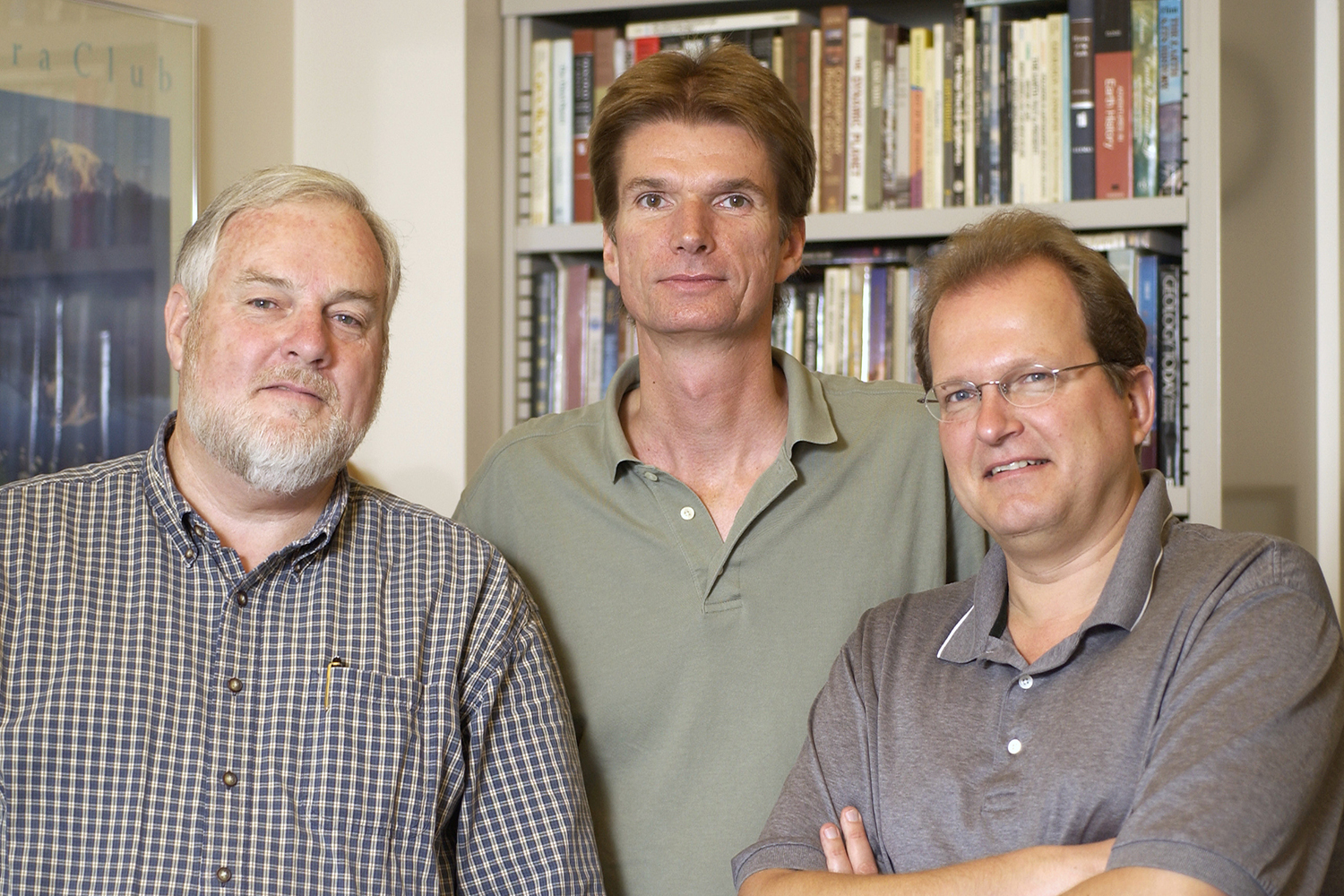 Gordon Brown and two of his colleagues pose together in an office, standing in front of shelves filled with books.