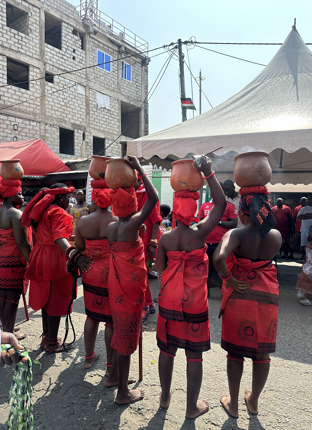 Photo of women and girls dressed in red and carrying ceremonial pots on top of their heads at the Ga Homowo Festival in Accra, Ghana.