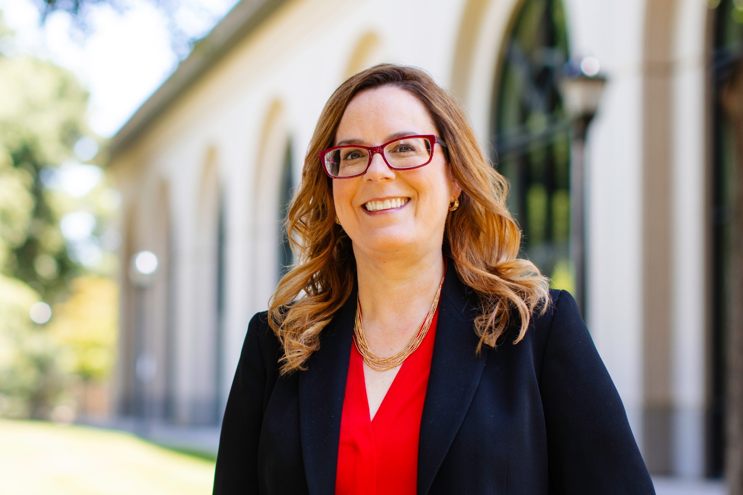 Jennifer Cochran posing for a profile photo outdoors with a building featuring arched windows in the background.