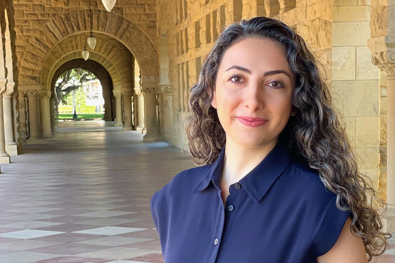 Asserian with curly hair standing in an in an arcade of the Quad.