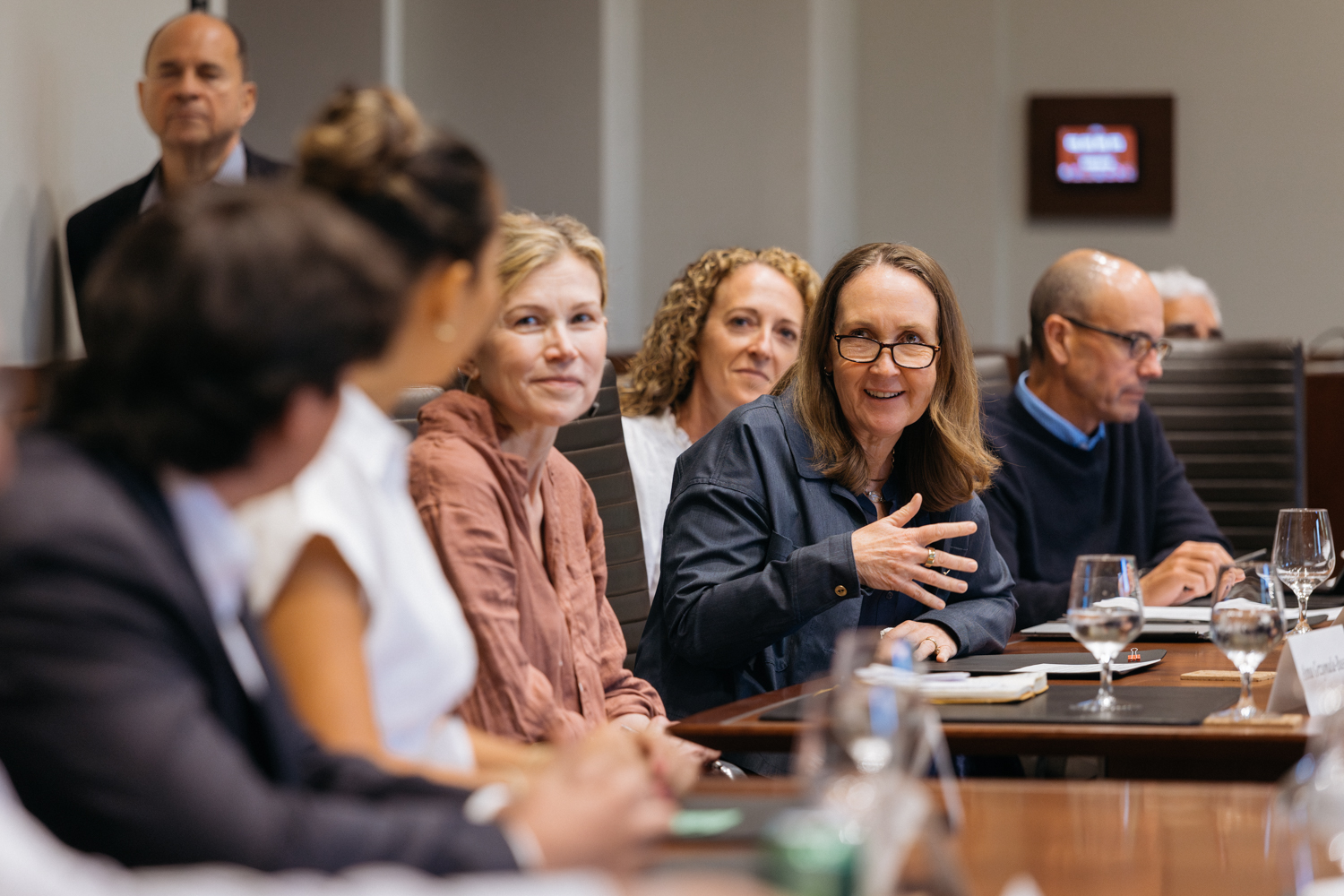 A group of people is engaged in a discussion around a conference table, with Provost Jenny Martinez speaking animatedly.