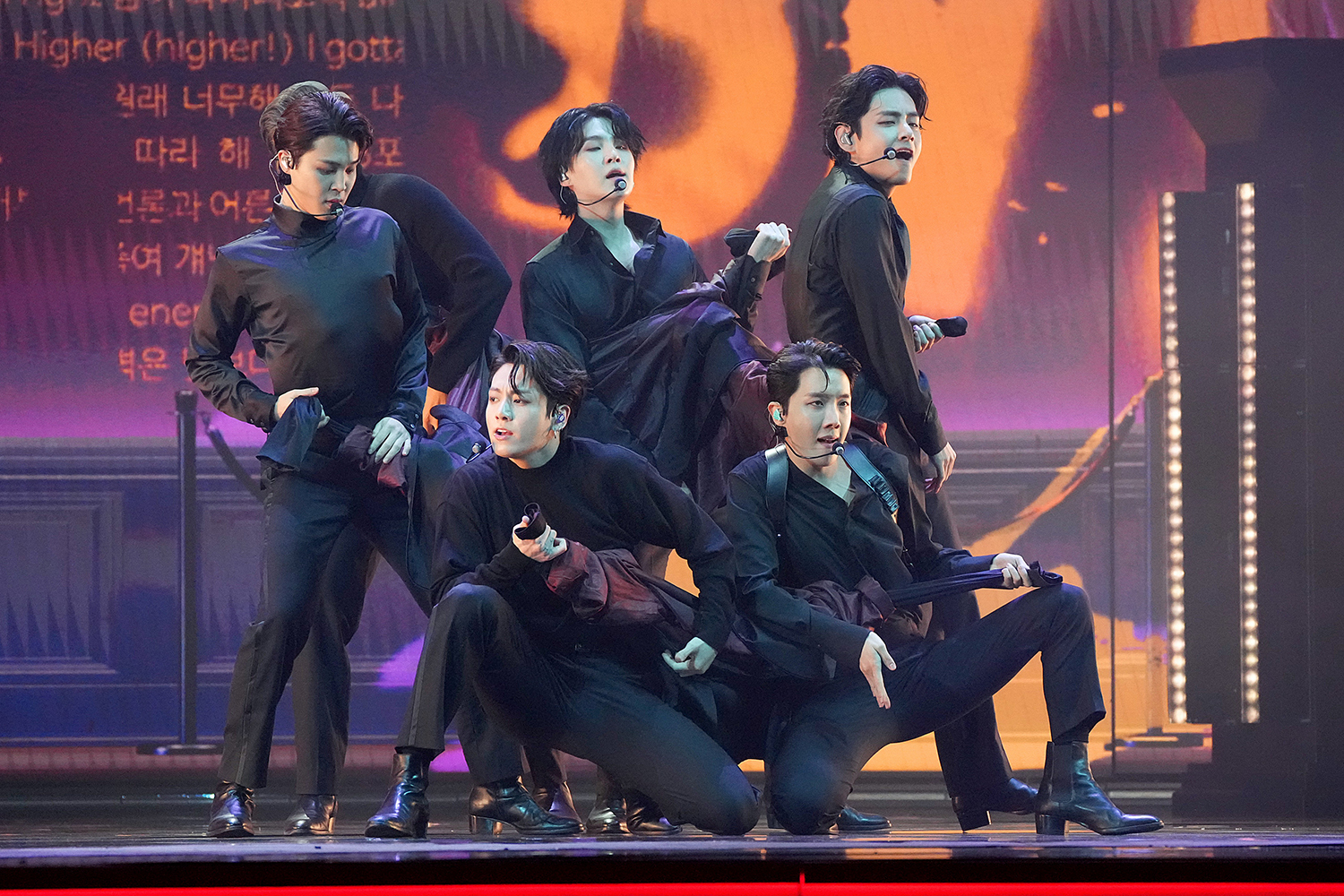 BTS performs on stage in coordinated outfits, showcasing dynamic poses with dramatic lighting in the background.
