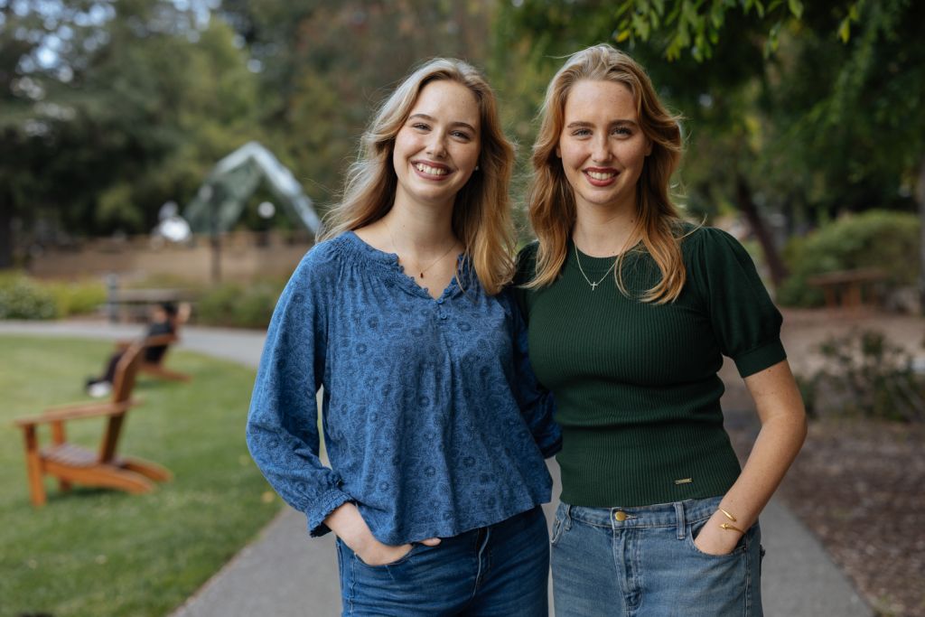 Open video Twin young women with long blond hair stand outside smiling on a sunny day. in a modal