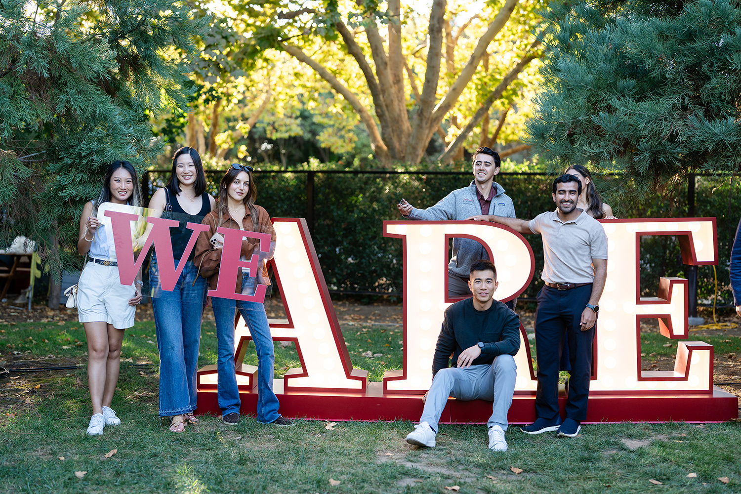 Members of the Stanford GSB community pose with giant letters spelling out WE ARE.