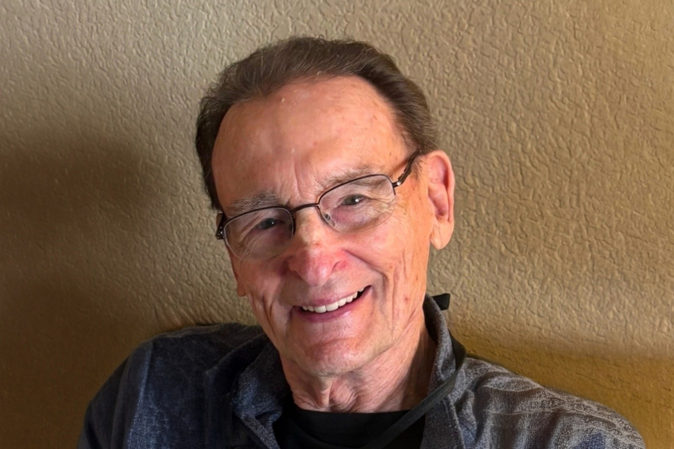 Zboralske with glasses smiling warmly while seated against a textured wall.
