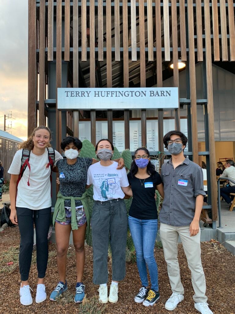 Five students posing with their arms around each other in front of a building with a sign that says Terry Huffington Barn