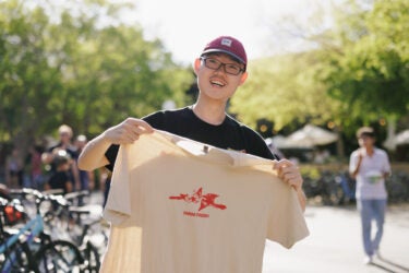A student holding a tan t-shirt with a red logo in the middle signifying Farm Day.
