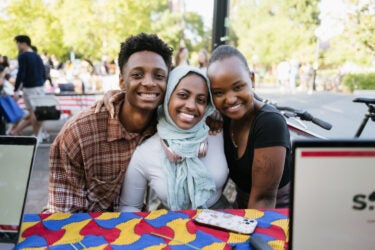 Three smiling students staffing a table