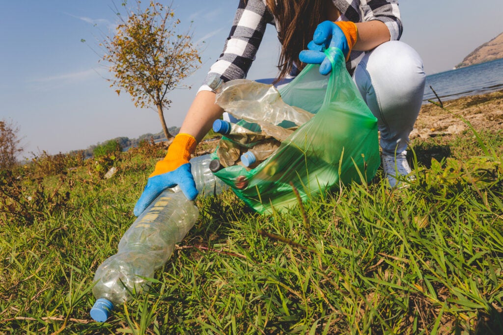 A woman's gloved hand is picking a plastic water bottle up from the grass