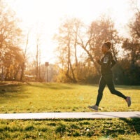 Woman jogging on a sunny path with grass behind her.