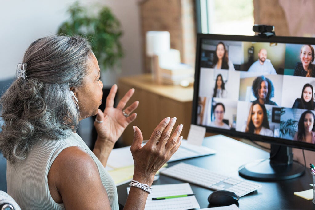 A senior businesswoman gestures as she facilitates a staff meeting while working from home. She is talking with her colleagues during a video conference.