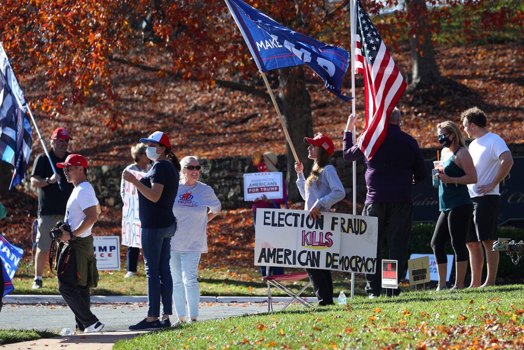 Protesters waving Trump and American flags hold a sign that reads "Election fraud kills American democracy."