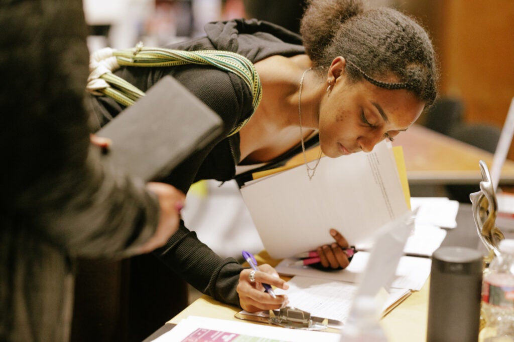 Student at a table writing on a sign-up sheet in a room with crowds behind her attending a career fair at Tresidder Memorial Union, Feb. 9, 2023.