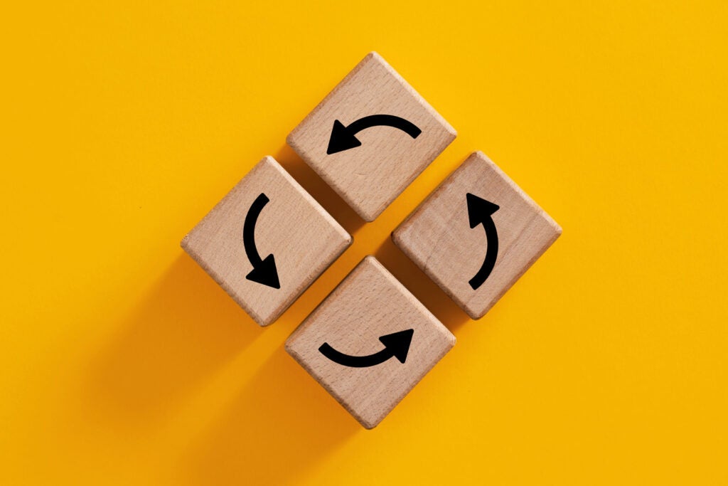 Photo of 4 wood blocks on a yellow background, with arrows on them indicating a circular, repeating pattern.