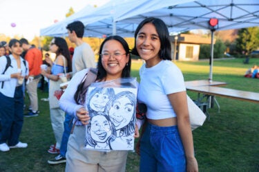 Two students holding a caricature of themselves and a third friend.