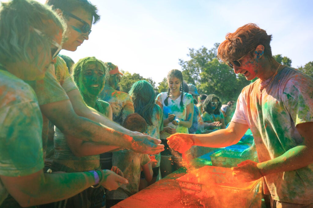 Students picking up handfuls of colored dust from bins on a table.