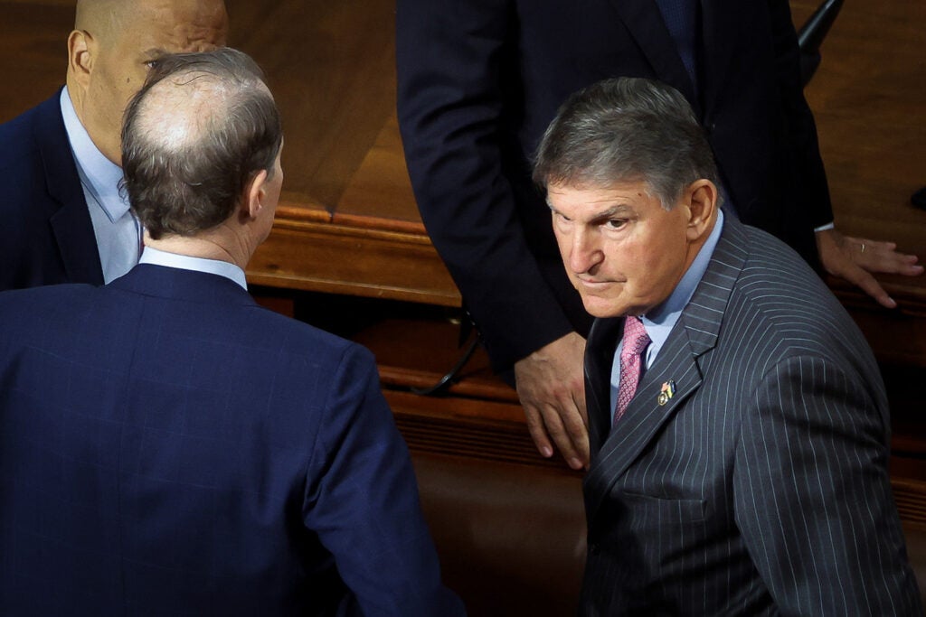 Senator Joe Manchin looks to his left while standing in a group with other lawmakers.