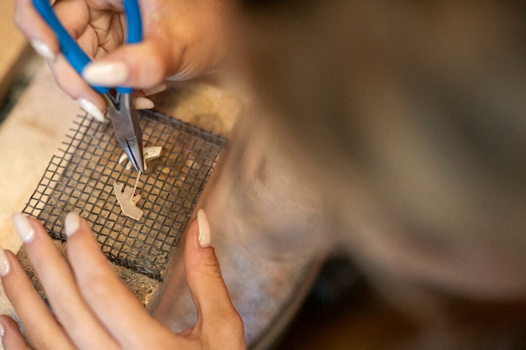 Closeup of student hands using pliers to work on a piece of jewelry.
