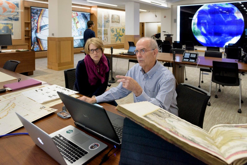 cartographic specialist and donor of the maps working at a desk covered with maps and computers