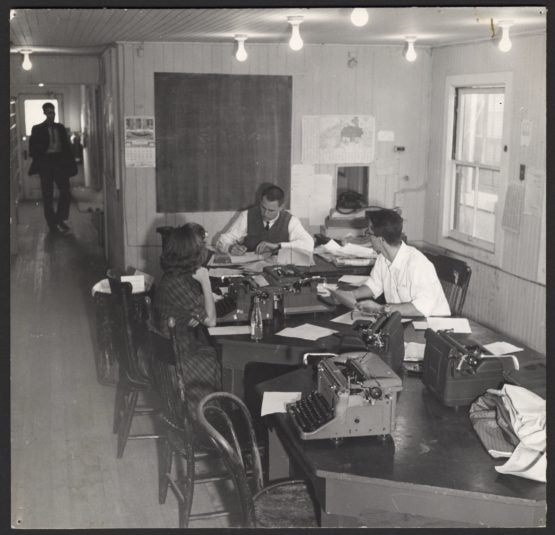 Black and white image of students around table working on typewriters. 