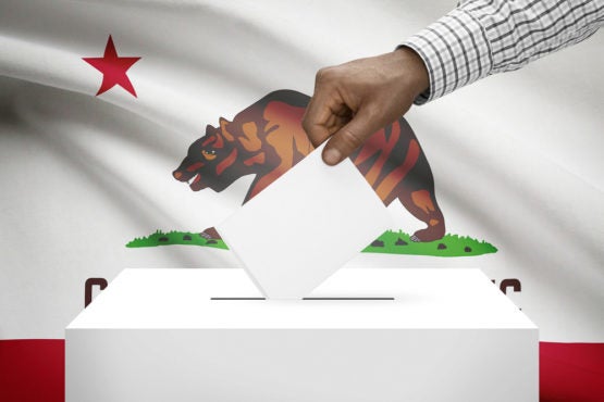 hand putting a ballot in ballot box with California flag in background