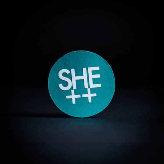 Teal felt circle with "SHE ++" written on it in white