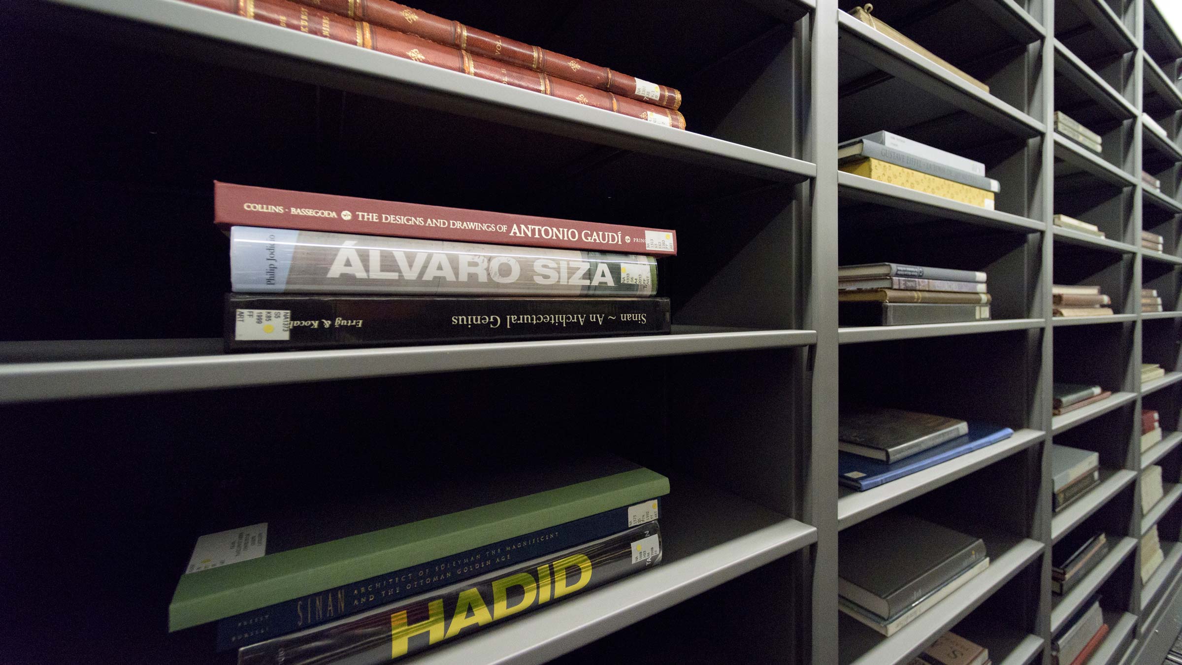 Large art books, lying horizontal on the narrow shelves of a gray bookcase. One of the books is black, with its title, Hadid, emblazoned in bold gold letters on its spine. (Image credit: L.A. Cicero)
