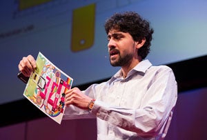Manu Pakrash holds an origami-stype paper microscope on stage at TED