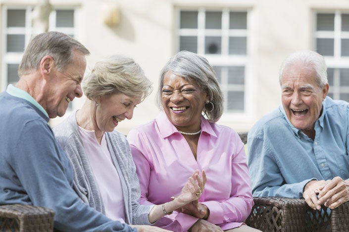 four multi-ethnic seniors sitting together outdoors, talking and laughing