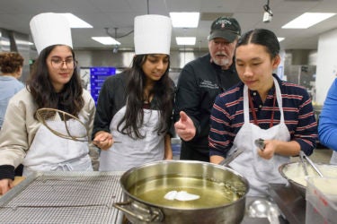 students and chef at the stove heating a pan of oil