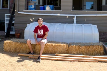 Student Andrew Jacobs sits on a water catchment system behind a house