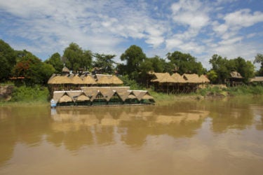 huts on the bank, and partially submerged in, a muddy river
