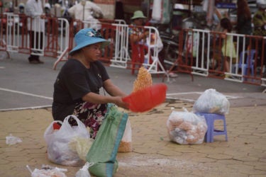 a woman seated on the ground, tossing corn in large plastic bowl