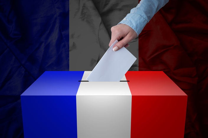 hand inserting a ballot into box decorated with French tricolor