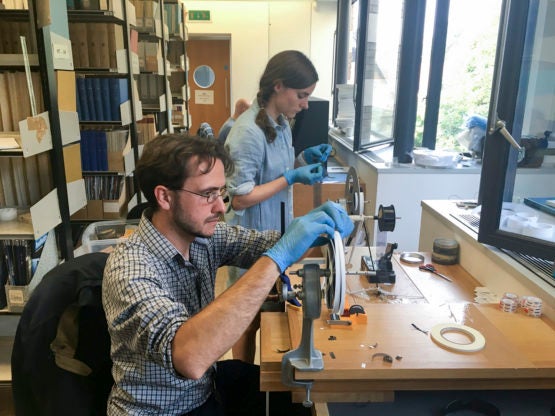 Professor Dustin Schroeder (foreground) and art historian Jessica Daniel splice 50-year-old film containing radar measurements of Antarctica into a reel in preparation for digital scanning at the Scott Polar Research Institute in the UK.