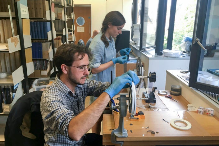 Professor Dustin Schroeder (foreground) and art historian Jessica Daniel splice 50-year-old film containing radar measurements of Antarctica into a reel in preparation for digital scanning at the Scott Polar Research Institute in the UK.)