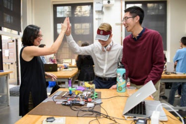 Professor Alison Okamura, left, celebrates a successful project with freshmen Brad Immel and Tiger Sun who worked on a team with Jonathan Sosa to create a Virtual Gear Shifter.