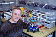 Steven Paley sitting at a work bench covered in engineering parts