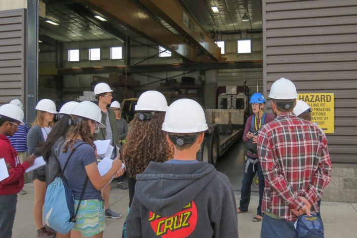 Students in hard hats stand outside a warehouse)