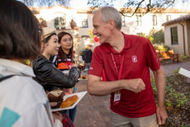 Stanford President Marc Tessier-Lavigne bumps elbows with frosh whose hands are full.