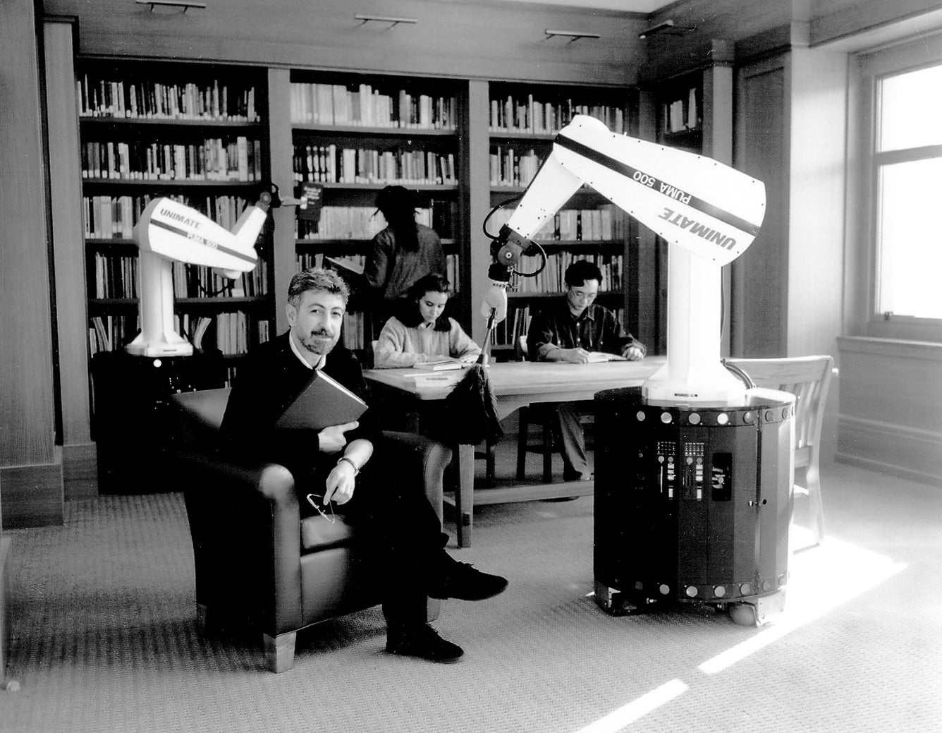 Khatib sitting in a library with two robot arms