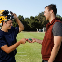 A man hands a football player a mouthguard.