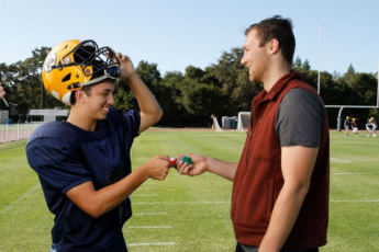 A man hands a football player a mouthguard.