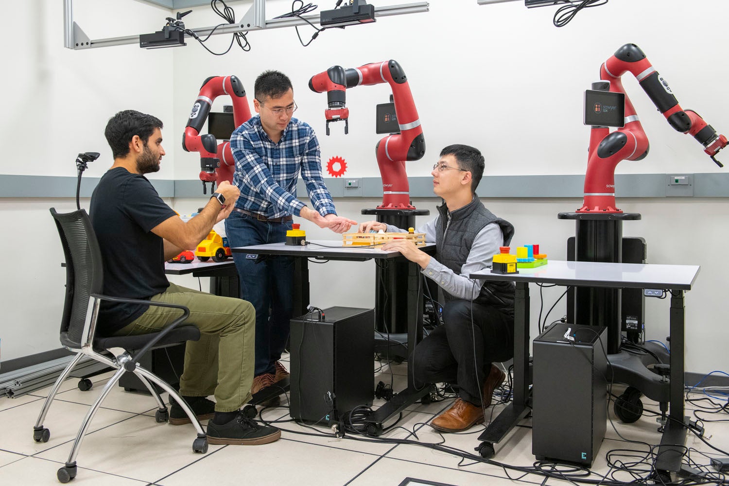 Using a handheld device, Ajay Mandelkar, Jim Fan and Yuke Zhu use their software to control the robot arm.